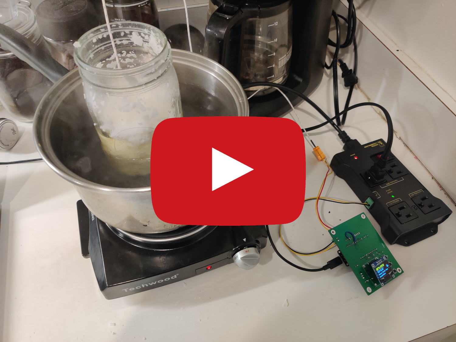 Jar of white flakey wax in a pot of water ontop of hot plate. Thermocouple from board inside of wax, where the board is connected to the relay control unit the board is connected into